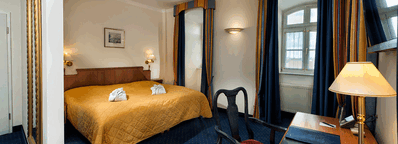 Ein klassisches Hotelzimmer mit einem großen, gelben Bett, stilvollen Vorhängen und einem Schreibtisch mit Lampe.