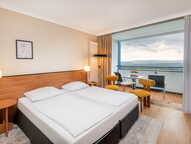 A modern hotel room with twin beds and a balcony overlooking a scenic landscape, featuring stylish decor and warm lighting.