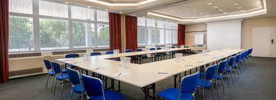 A spacious conference room with blue chairs and U-shaped tables ready for a meeting at Ehrenbreitstein.
