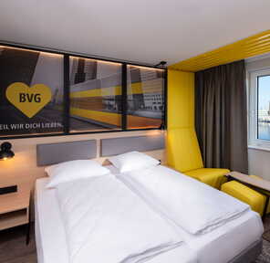 Ein modernes Berliner Hotelzimmer mit gelbem Sessel und Blick auf den Fluss durch das Fenster.