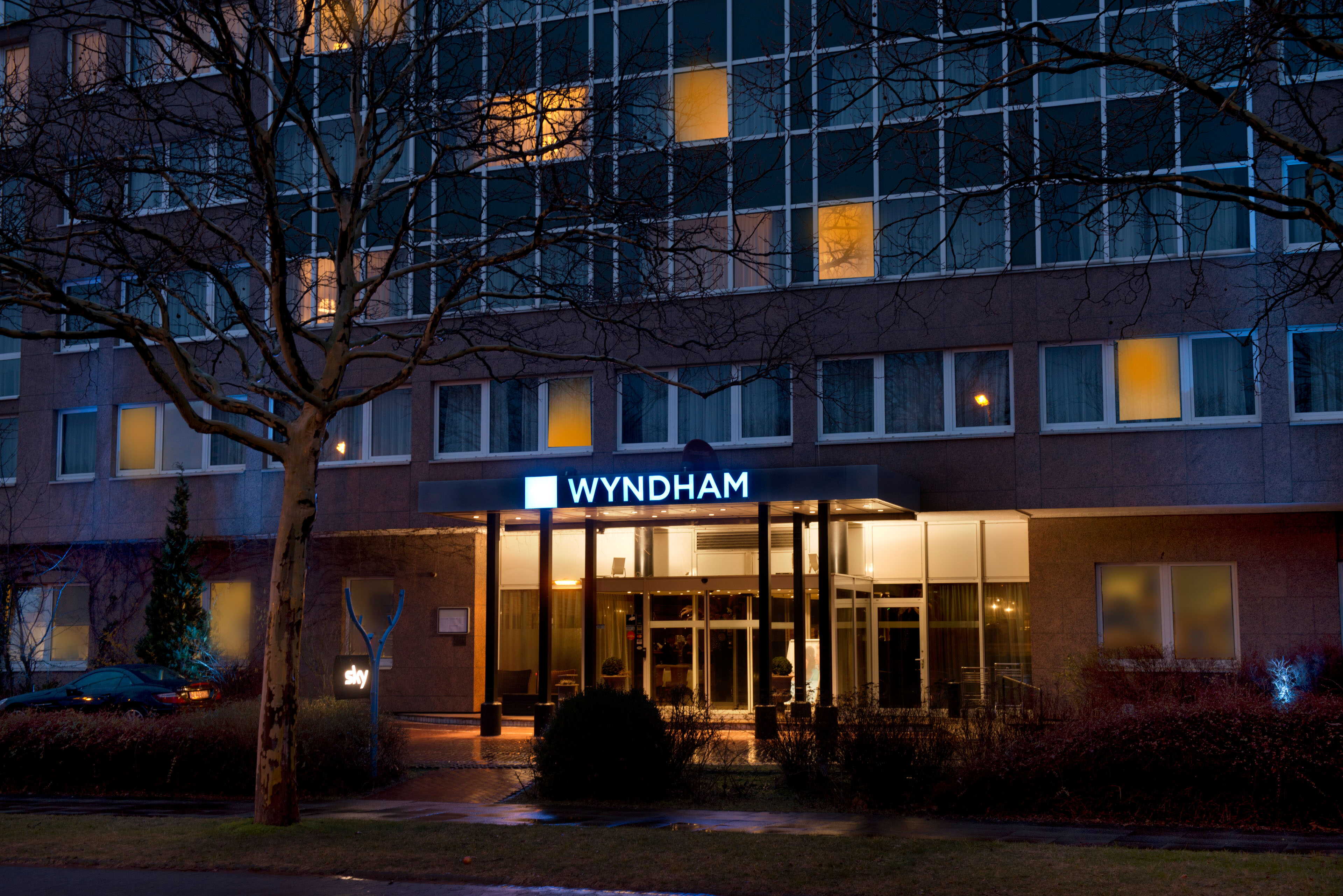 The illuminated exterior of a Wyndham hotel at night showcases inviting entrance lights amidst a darkened urban setting.