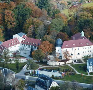 An aerial view showcases a picturesque estate surrounded by vibrant autumn trees and a winding road.