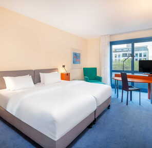 Ein modernes Hotelzimmer mit Doppelbett, Schreibtisch und Fernseher bietet einen Blick auf die Stadt durch ein großes Fenster.