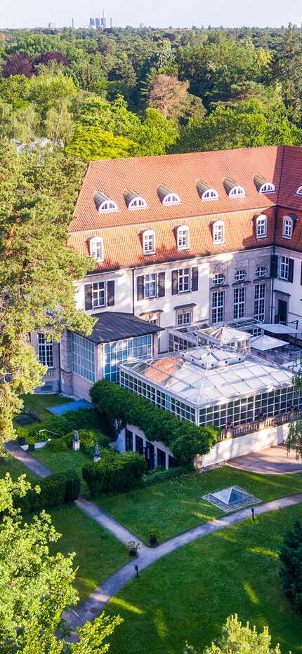 Ein großes Gebäude mit rotem Dach ist von üppigen Bäumen umgeben und steht inmitten eines grünen Parks.