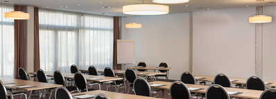 Ein moderner Meetingraum mit Tischen und Stühlen ist für eine Präsentation vorbereitet, mit einem Flipchart im Hintergrund.