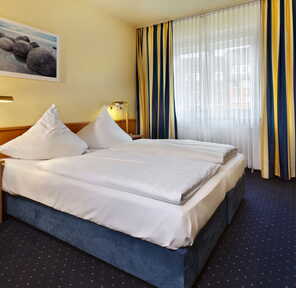 Gemütliches Doppelzimmer mit blau-gelben Vorhängen, einem großen Bett und einem Bild von Steinen an der Wand.