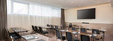 Ein moderner Meetingraum im Flachgau mit Tischen, Stühlen, Notizblöcken und einem großen Bildschirm an der Wand.