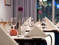 Elegantes Restaurant mit gedeckten Tischen, weißen Servietten und dekorativen Blumenvasen für ein stilvolles Dinner.