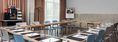 A conference room is set up with a U-shaped table arrangement, complete with notepads, pens, and glasses for a meeting.