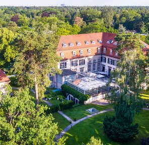 Aerial view of a historic building surrounded by lush greenery, showcasing its red roof and elegant architecture.