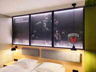 A cozy room features a bed with overhead sports-themed decor and a "Füchse Berlin" logo illuminated by modern lighting.