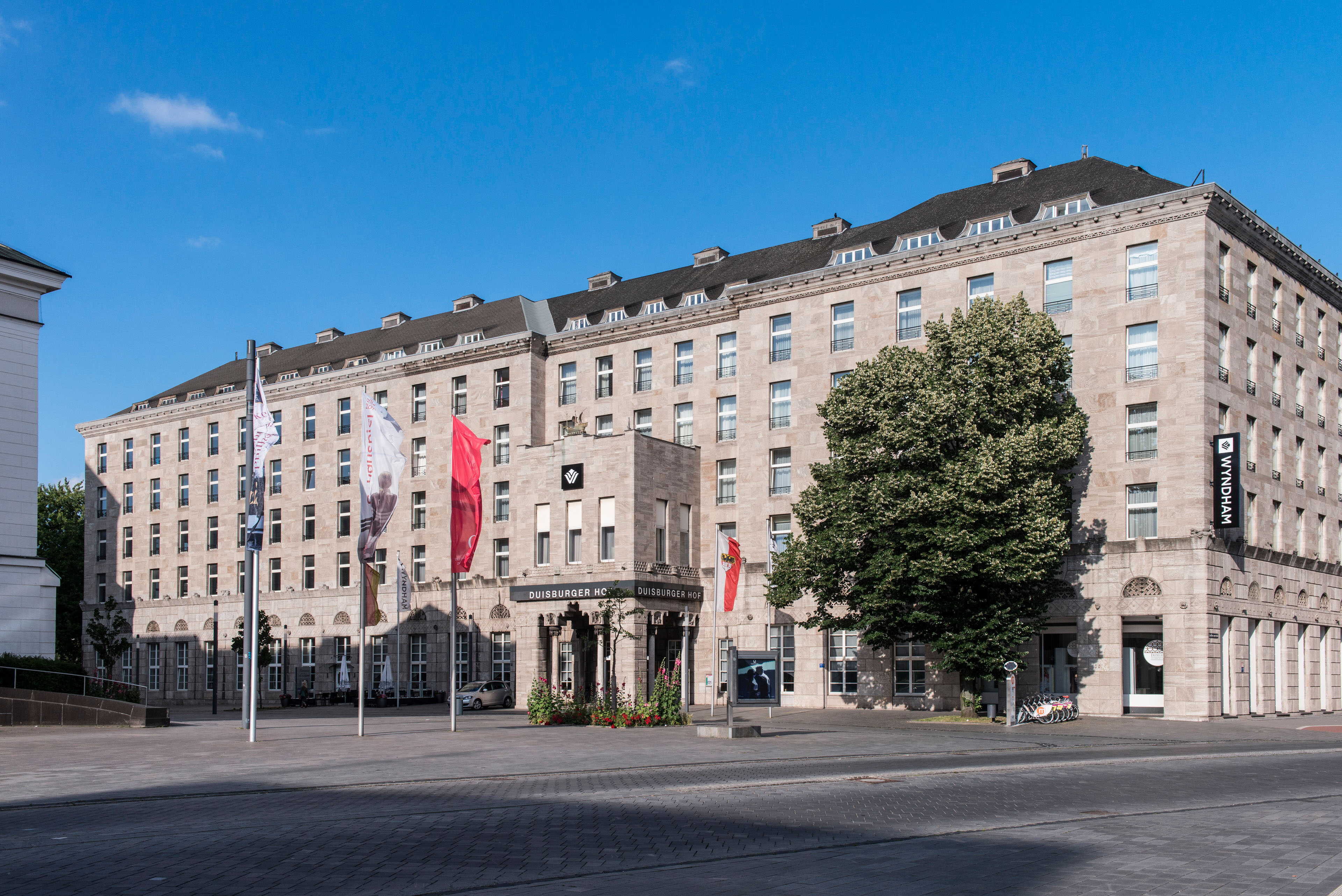 The Duisburg building exterior features classic architecture with flags and a tree under a clear blue sky.