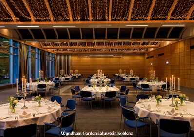 Ein elegant dekorierter Festsaal mit runden Tischen, Kerzenleuchtern und Lichterketten an der Decke.