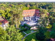 Aerial view of a historic building surrounded by lush greenery, showcasing its red roof and elegant architecture.