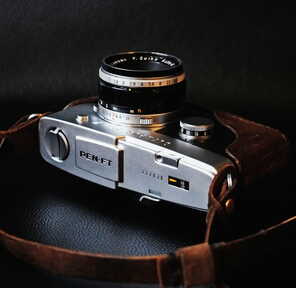 Eine klassische PEN-FT Kamera liegt mit einem braunen Lederriemen auf einem dunklen Hintergrund.